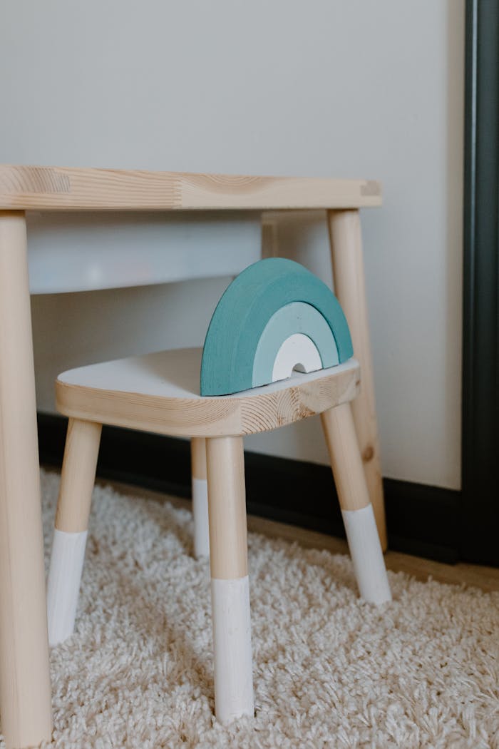 Wooden childrens chair with blue accent beside a matching table on a carpeted floor.